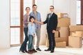 Realtor with family in new apartment with cardboard boxes. Father and realtor are shaking hands.