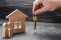 The realtor`s hand holds the keys to the house. A wooden house and a family with a child. The concept of buying and selling