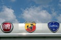 Fiat, Abarth and Lancia logos in the dealership of the area, against a blue sky with clouds. They are all part of the Fiat Group