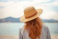 Rear back view ginger haired lady in straw hat enjoying summer day by sea shore. AI generative