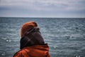 Rear close-up view of a person in an orange hat and checkered scarf watching the undulating sea