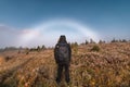 Rear of male traveler adventure standing on golden meadow with fog bow or white rainbow on autumn forest in Assiniboine provincial