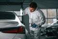 Rear part of automobile. Garage worker is holding lighting and checking surface of the car