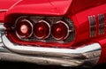 Rear Part Of Exterior Of A Red Old Timer Luxury Sports Car With Tree Tail Lights Framed In Chrome Nozzles, Shiny Chrome Bumper And
