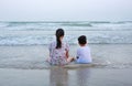 Rear of peaceful Asian young girl child and little boy sitting on tropical sand beach at sunset. Family of sister and brother in Royalty Free Stock Photo