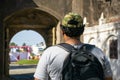 Rear portrait of young Indian traveler with backpack and cap looking at the perimeter wall of a fort in India