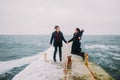 Rear romantic view of a young couple walking together with little dog and having fun on stoned pier during rainy autumn