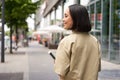 Rear shot of young woman walking in city, going down the street and smiling, holding smartphone. View from behind Royalty Free Stock Photo