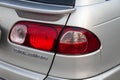 Rear taillamp view of Toyota Caldina car of 2000 release in the back of a silver T210 station wagon in a parking lot with a green