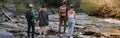 Rear on two couples standing hand in hand at river on rocks. Hikers in mountains valley. Royalty Free Stock Photo