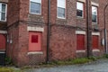 Rear of an urban apartment building, lower windows blocked with red painted boards