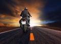 Rear veiw of young man riding big motorcycle on asphalt road against beautiful dusky sky