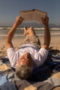 Senior man reading a book while relaxing on picnic blanket at beach Royalty Free Stock Photo