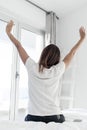 Rear view of a Adult woman outstretching her arms sitting on the bed after good night sleep Royalty Free Stock Photo