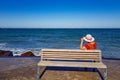 Rear view of an adult woman sitting on wooden bench on boardwalk with sea and horizon in background Royalty Free Stock Photo