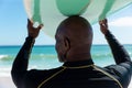 Rear view of african american bald senior man carrying surfboard on head at beach Royalty Free Stock Photo