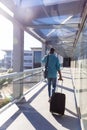 Rear view of african american businessman walking with luggage in corridor at airport on sunny day Royalty Free Stock Photo