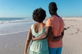 Rear view of african american couple standing with arms around at beach during summer holiday Royalty Free Stock Photo