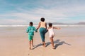 Rear view of african american grandmother holding boy and girl\'s hands running at beach against sky Royalty Free Stock Photo