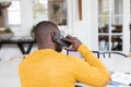 Rear view of african american man using laptop at home and talking on smartphone Royalty Free Stock Photo