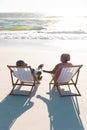 Rear view of african american senior couple sitting on deckchairs at beach in front of sea under sky Royalty Free Stock Photo