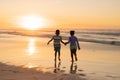 Rear view of african american siblings holding hands and running on beach against sky at sunset Royalty Free Stock Photo