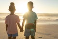 Rear view of african american siblings holding hands while watching sunset over sea from beach Royalty Free Stock Photo