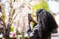 Rear view of african american tourist woman visiting a picturesque city street destination, using a smart phone taking pictures on Royalty Free Stock Photo