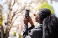 Rear view of african american tourist woman visiting a picturesque city street destination, using a smart phone taking pictures on Royalty Free Stock Photo