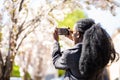 Rear view of african american tourist woman visiting a picturesque city street destination, using a smart phone taking pictures on Royalty Free Stock Photo