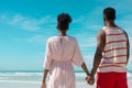 Rear view of african american young couple holding hands and looking at sea while standing on beach Royalty Free Stock Photo