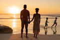 Rear view of african american young couple looking at playful children running on beach against sky Royalty Free Stock Photo