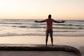 Rear view of african american young man with arms outstretched standing at beach against clear sky Royalty Free Stock Photo