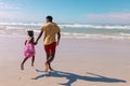 Rear view of african american young man and daughter holding hands and running at beach against sky Royalty Free Stock Photo