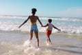 Rear view of african american young mother holding girl's hands and enjoying in sea against sky