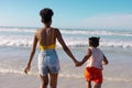 Rear view of african american young woman holding daughter's hands and running in sea against sky Royalty Free Stock Photo