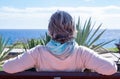 Rear view of an aged grey-haired woman relaxing in front to the sea sitting on a bench looking at the horizon. Senior woman