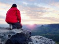 Rear view of alone hiker in dark red outdoor clothes sitting on rock.