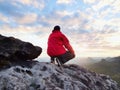 Rear view of alone hiker in dark red outdoor clothes sitting on rock.