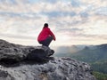 F alone hiker in dark red outdoor clothes sitting on rock. Sharp rocky peak