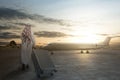 Rear view of an Arab man wearing keffiyeh walking with a suitcase for traveling by plane Royalty Free Stock Photo