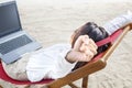 Rear view of asian business woman relax when working with laptop while using headphones sitting in the beach chair on beach Royalty Free Stock Photo