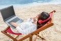 Rear view of asian business woman working with laptop while using headphones sitting in the beach chair and thinking something on