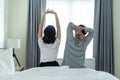 Rear view of Asian couple stretching hands after wakeup in morning. Attractive new marriage man and woman in pajamas feel happy