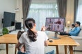 Rear view of Asian Female freelance worker work at home due Covid-19 with daughter on hands and family. Working business mother ta