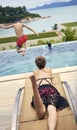 Rear view of Asian woman lying on stomach sunbathing on deck chair while kid jumping into pool