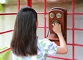 Rear view of Asian young girl kid using dial telephone booth. Child call on the retro vintage red phone booth Royalty Free Stock Photo