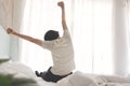 Rear view Asian Young man waking up stretching his arms while sitting on the bed during early morning at home or apartment on Royalty Free Stock Photo