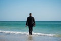 Rear view of back business man in suit in sea water at beach. Businessman tourist in casual suit barefoot walking on Royalty Free Stock Photo