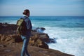 Rear view of backpacked man traveler tourist looking into the distance, standing on the cliff overlooking Atlantic ocean